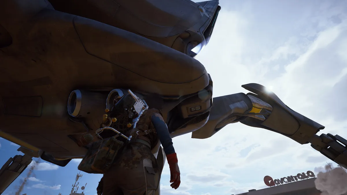 A raider stands directly under the Matriarch's armored belly and leg joint on a sunny day, looking up at the machine