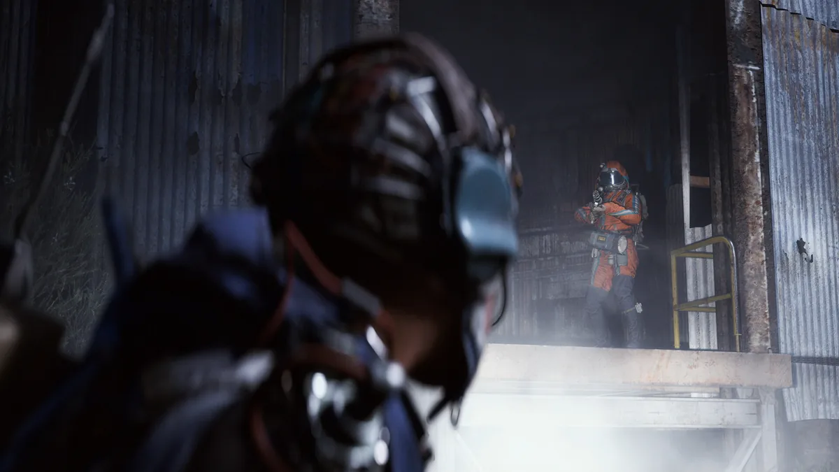 A Raider aims a pistol down a smoke-filled industrial corridor between rusted metal walls, with a second Raider blurred in the foreground