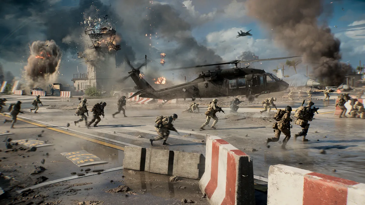 Marines running across a beach toward a burning helicopter and control tower under heavy smoke, with a fighter jet flying overhead