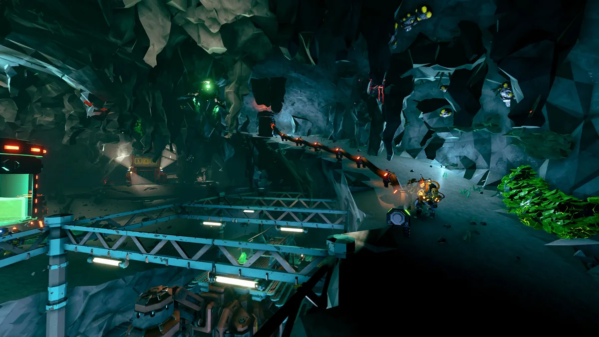 A cave environment with a mining terminal, overhead lighting rig, and floating drone lights near a rocky tunnel branch