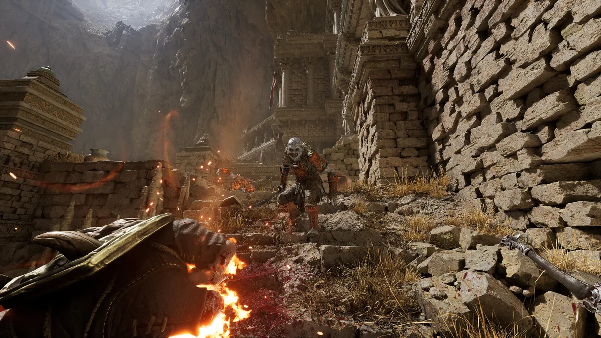 Fatekeeper first-person combat in dark stone ruins, fire illuminating the corridor and an enemy silhouetted ahead