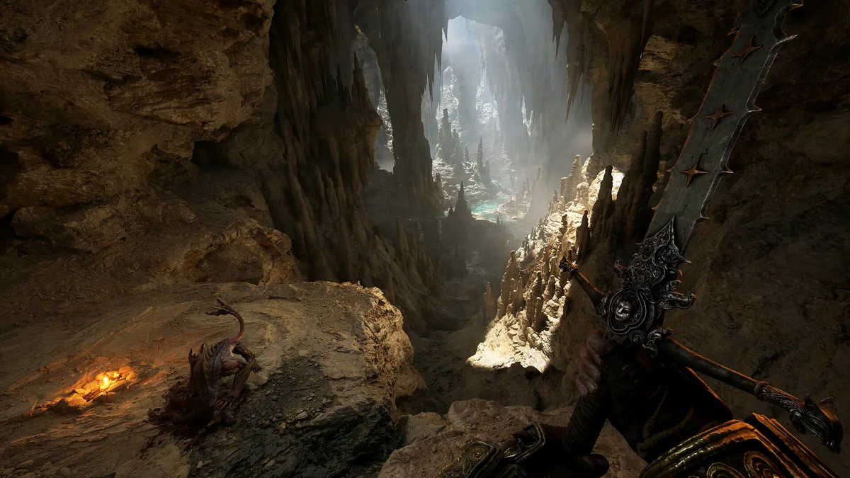 Fatekeeper first-person view inside a vast limestone cavern with light beams filtering through gaps, a stone path winding into shadow ahead