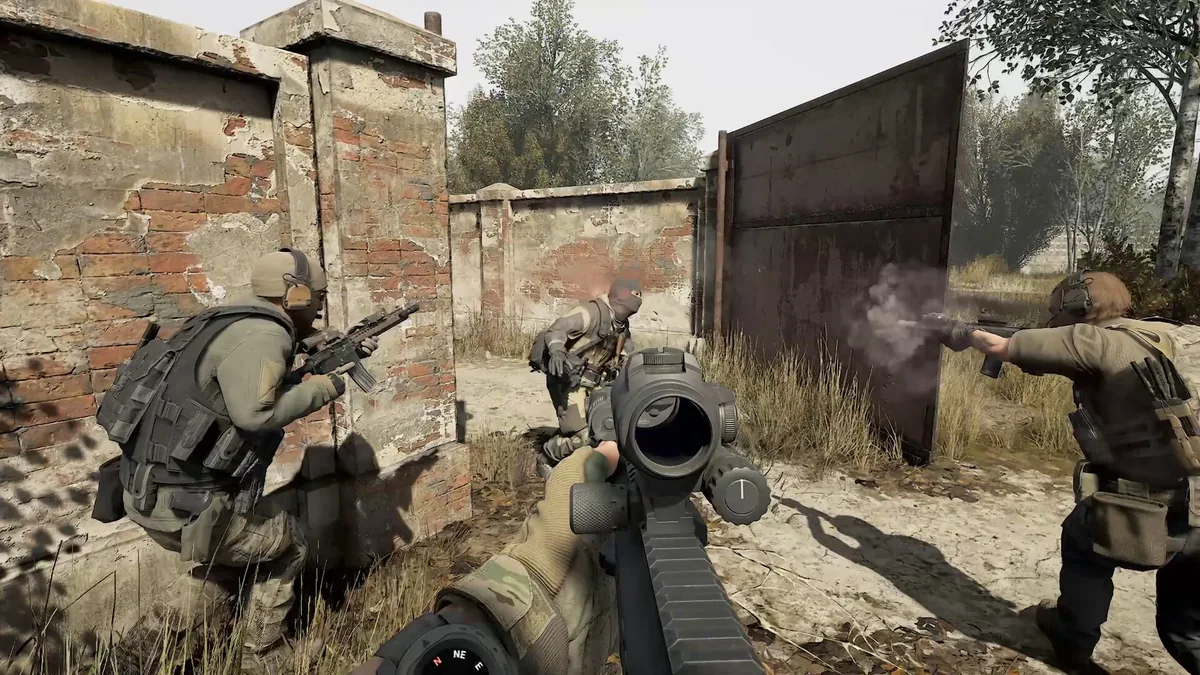A first-person view of an operator firing through a compound gate as two teammates take cover behind a brick wall