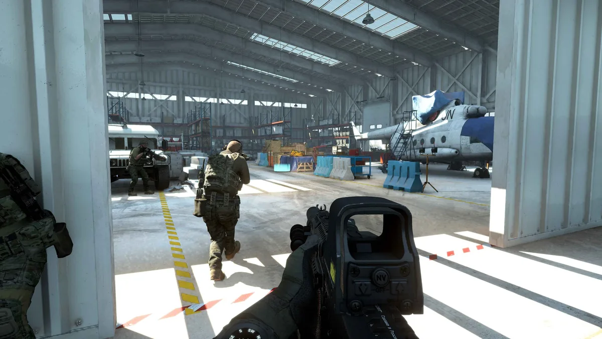 A first-person view inside an aircraft hangar with a covered plane and two teammates advancing past parked vehicles and cargo crates