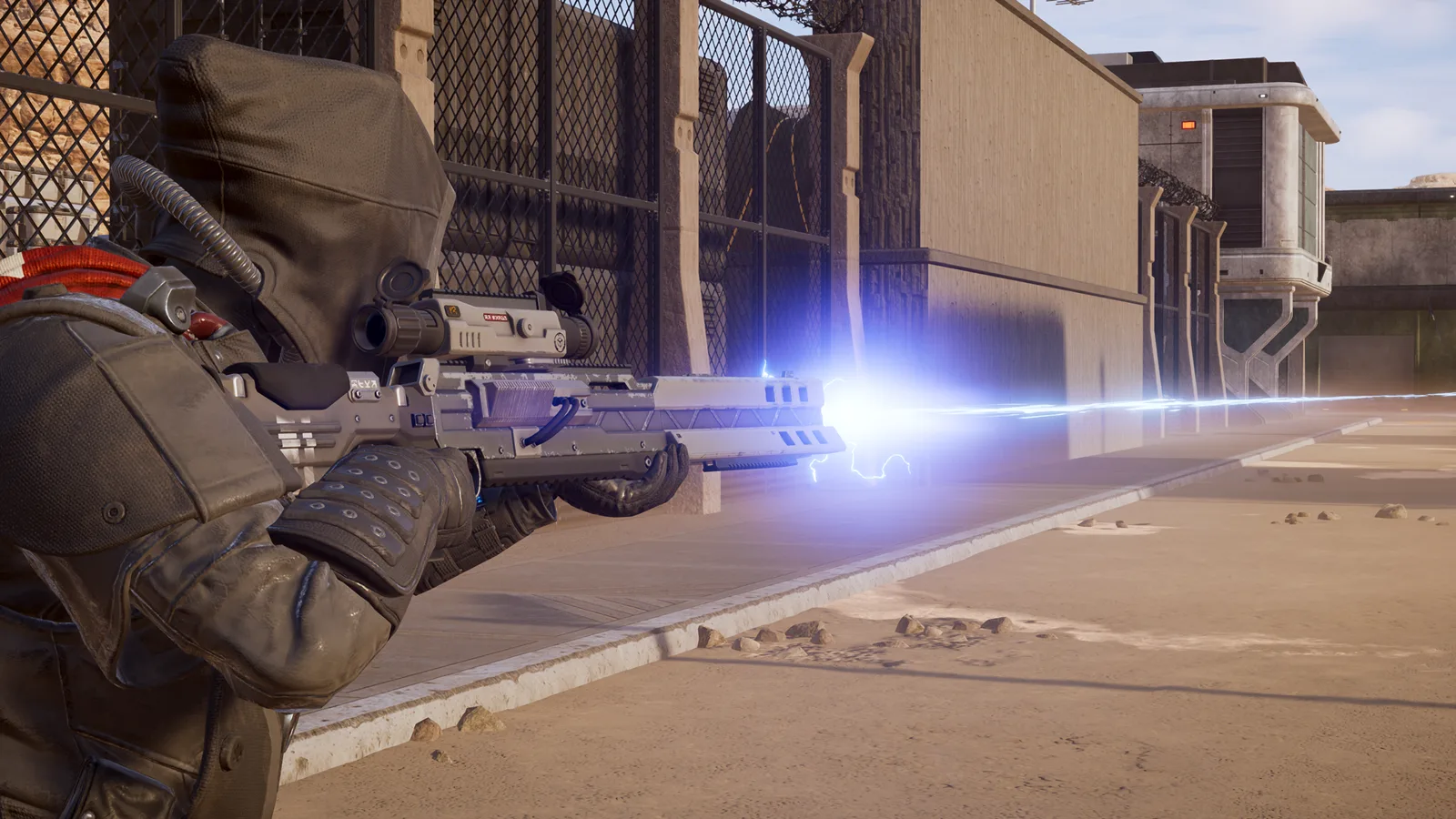 Hooded Helldiver in heavy armor firing a blue laser rifle along a desert compound wall