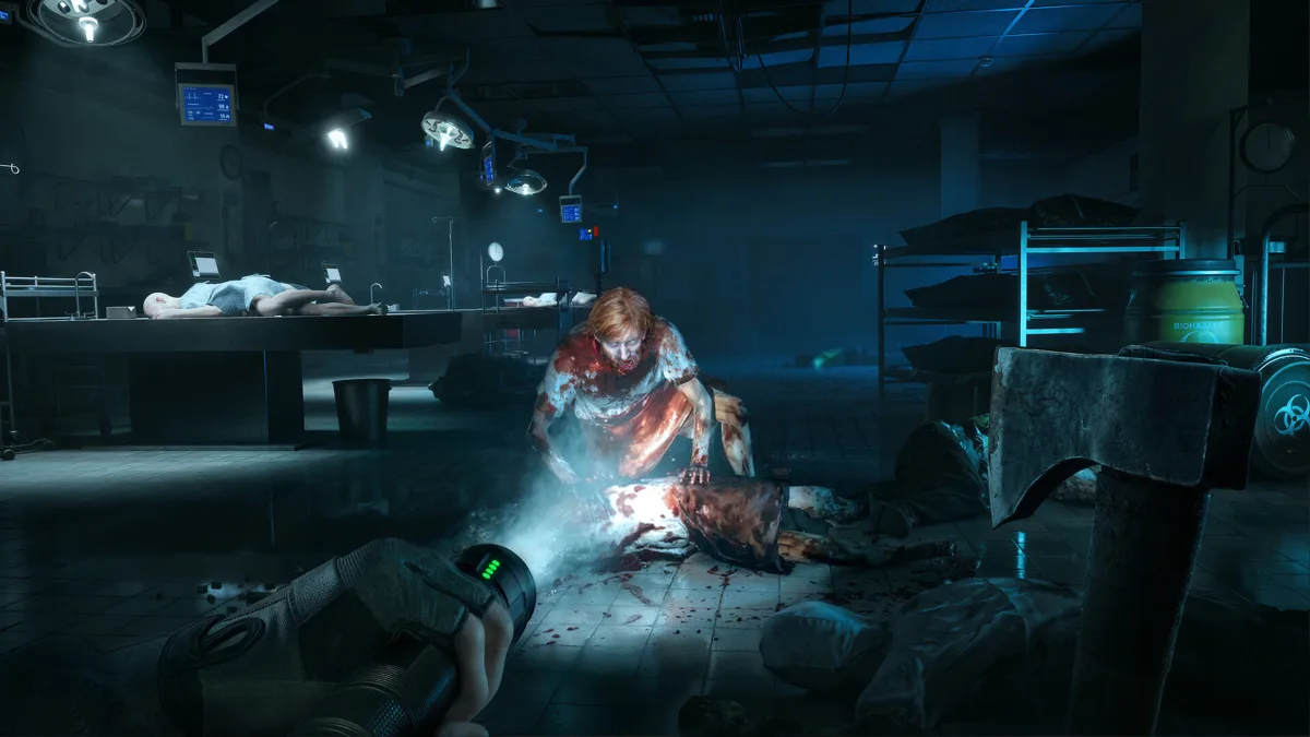 A flashlight beam picks out a bloodied zombie crouched over a body on a morgue floor while the player raises an axe