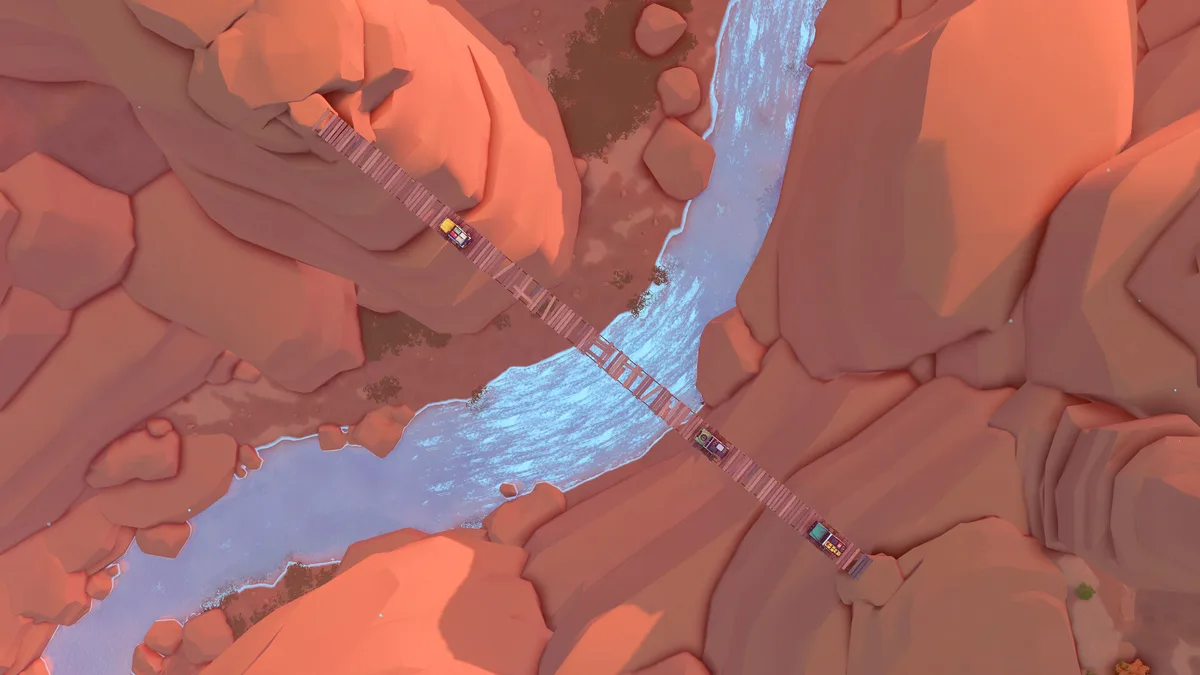 Top-down view of three 4x4s spaced out along a long plank bridge over a river in a red rock canyon