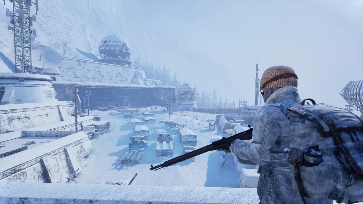 A bundled survivor looks across snow-covered buildings in a frozen town.