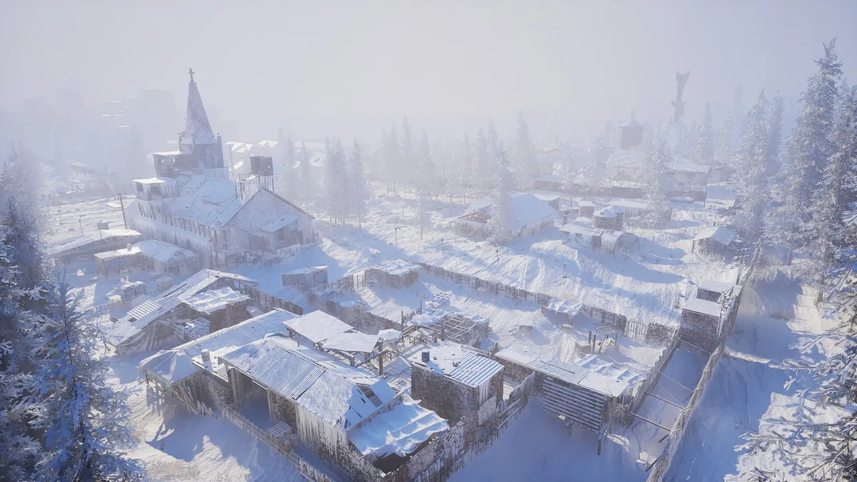 Aerial view of a snow-covered settlement with clustered buildings, fences, and trees.