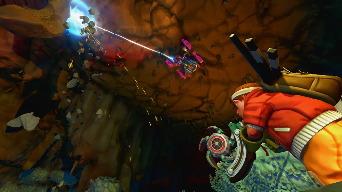 A small pink and blue armored mining vehicle hovers in a cave, cutting through rock with a blue laser beam