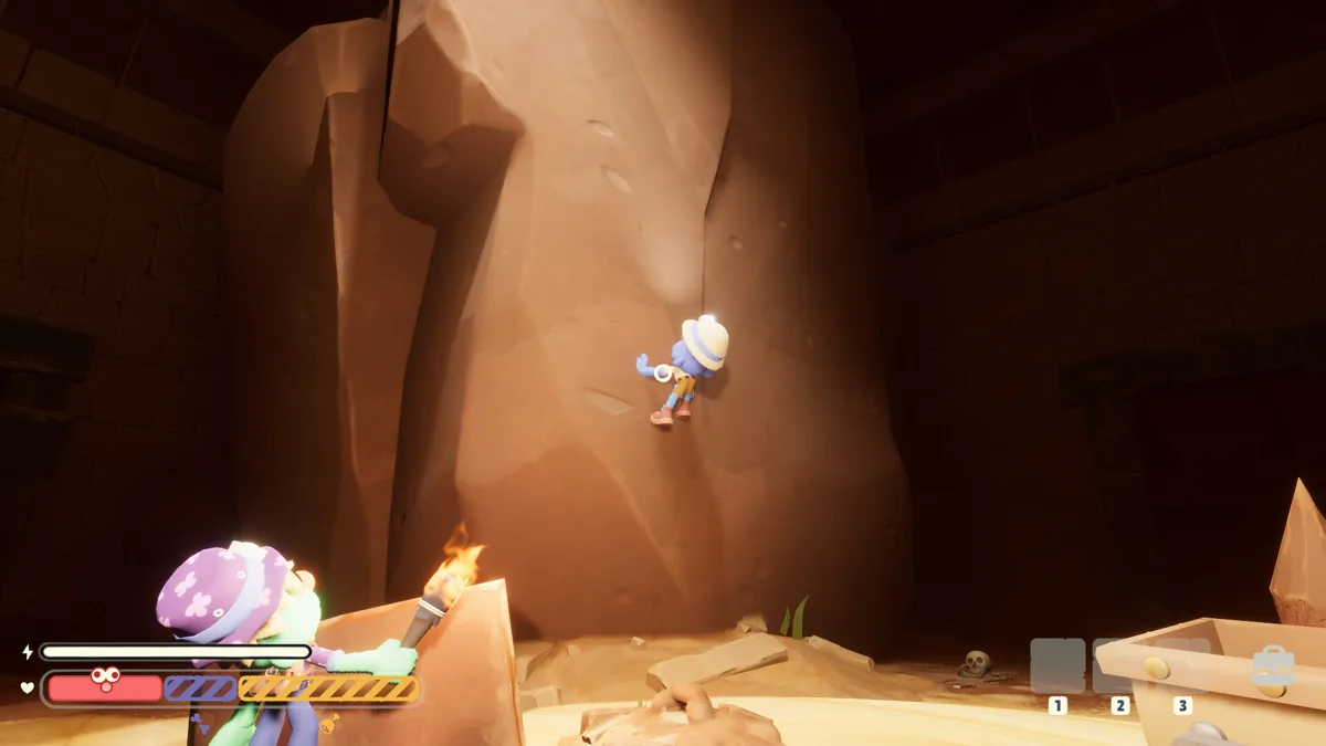 An explorer climbs a sheer sandstone rock face while a teammate in a purple polka-dot hat watches from below with a torch