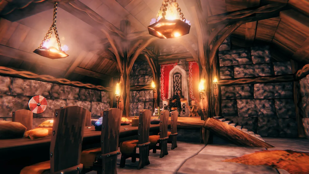 Valheim mead hall interior with a long table, cushioned chairs, hanging braziers and a seated figure at the far end