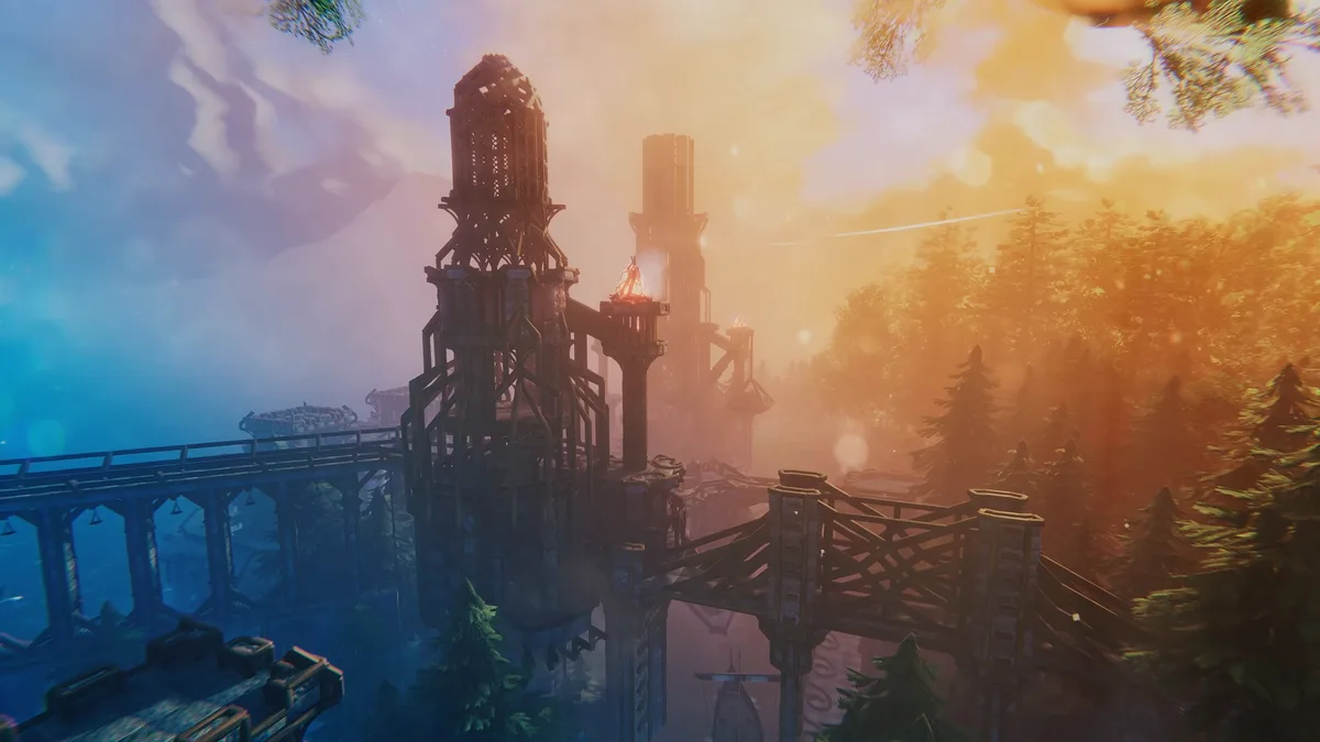 A tall wooden watchtower beside a long stone-arched bridge, lit by an orange sunset over a pine forest