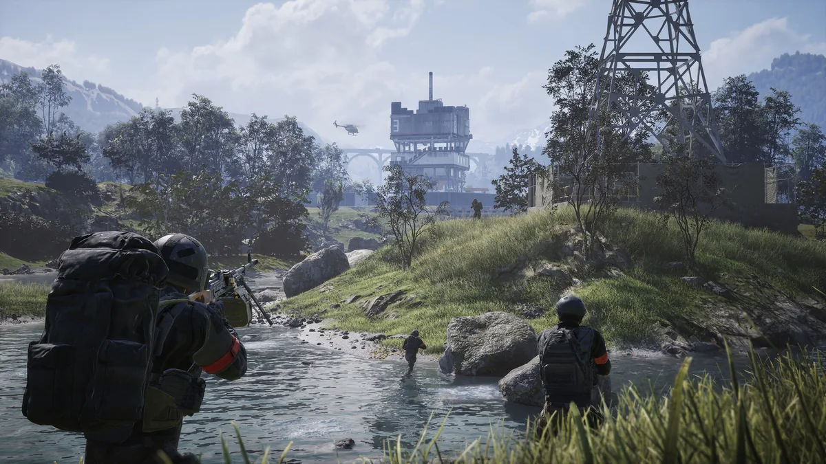 Three soldiers cross a shallow river toward a distant industrial tower objective with a helicopter flying overhead, one wearing a red team armband