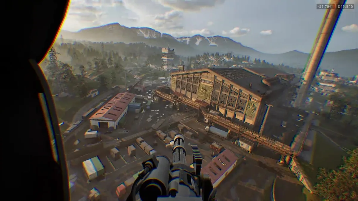 Aerial view from a door-gunner position over an industrial factory complex with tall smokestacks, warehouses, and surrounding mountains