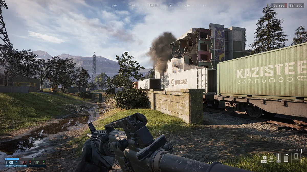 WARDOGS rifle view across a muddy industrial approach with a freight container, damaged building, power pylons, and mountains