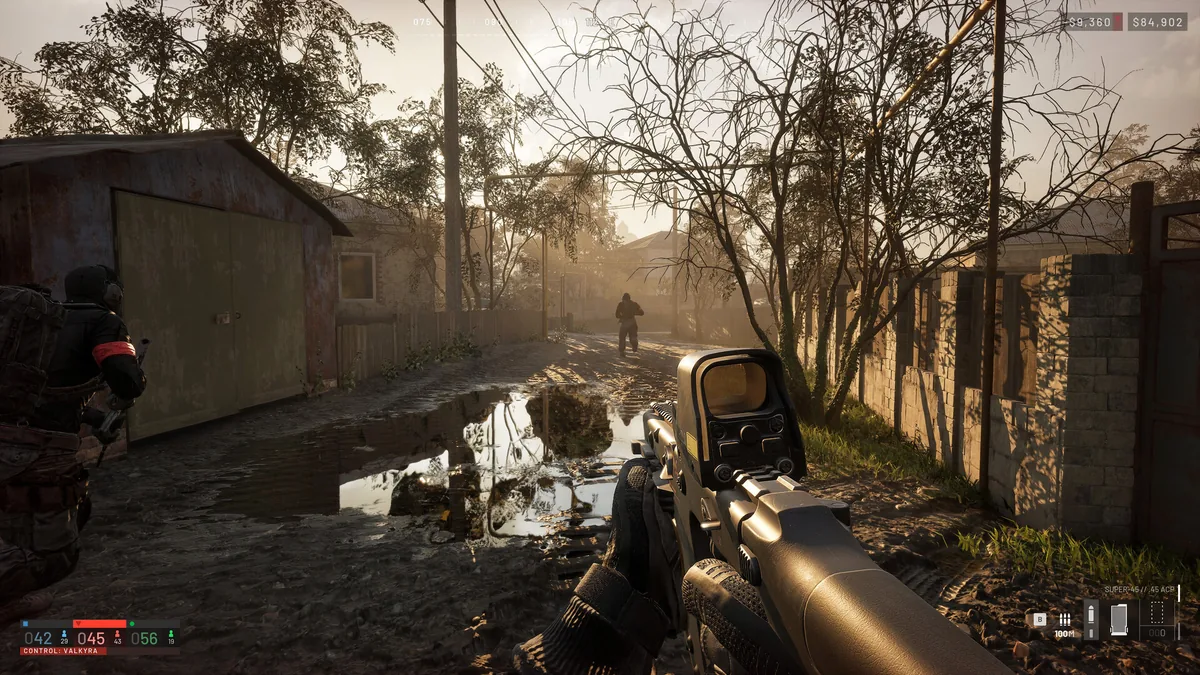 First-person WARDOGS view down a muddy residential lane with puddles, low walls, trees, and a teammate ahead
