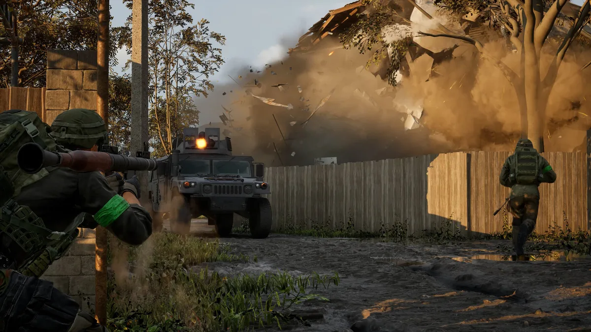 A soldier fires a rocket launcher at an armored Humvee while a building explodes into debris in the background, with a squadmate running toward the fence line