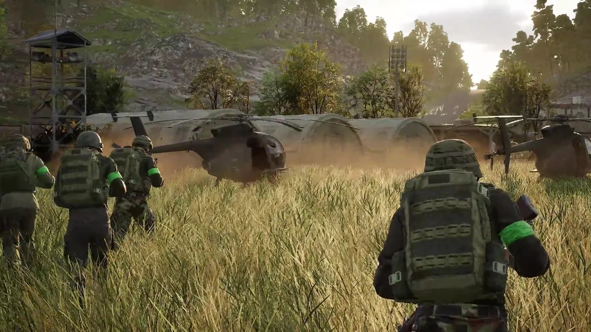 Soldiers run through tall grass toward two small MH-6-style helicopters idling near curved metal shelters, dust kicking up from the rotor wash